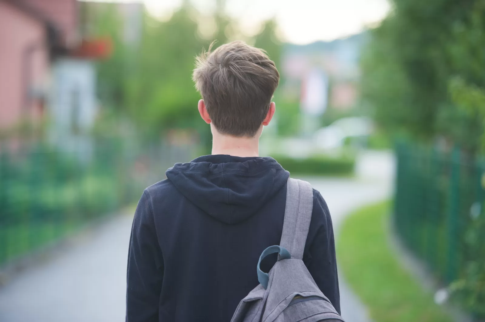 Tiener met rugzak loopt richting schoolgebouw